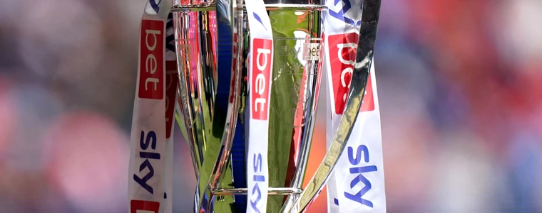 Cúp Champions League đặt trên bục dưới ánh đèn, phía sau là sân vận động về đêm minh họa cho vòng play-off mùa 2026/27